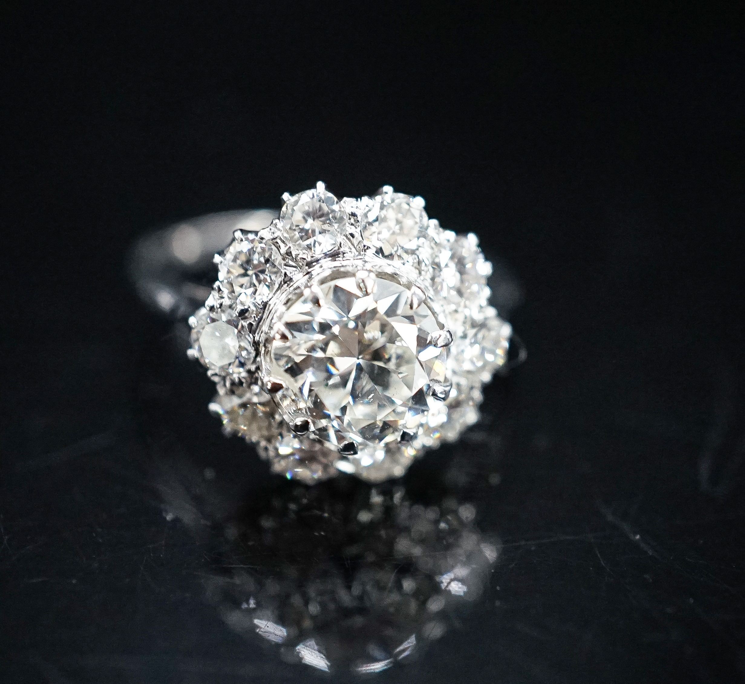 A white metal and eleven stone diamond set flower head cluster ring, the central stone weighing approximately 1.60ct, size N, gross 5 grams